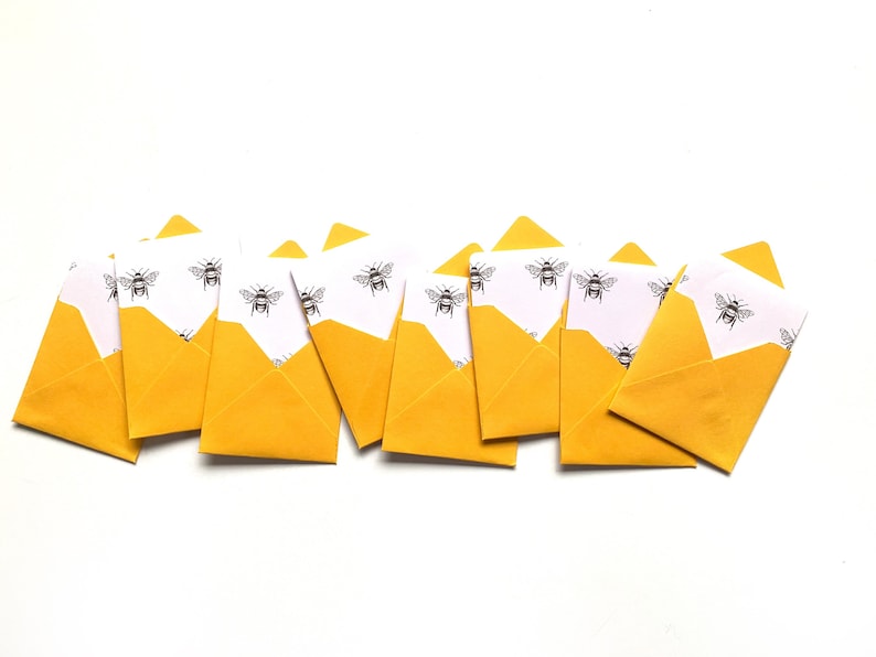 May include: A row of yellow envelopes with white paper inside, each decorated with a black and white bee pattern.
