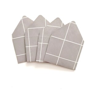 May include: Four gray paper envelopes with a white grid pattern. The envelopes are stacked on top of each other.