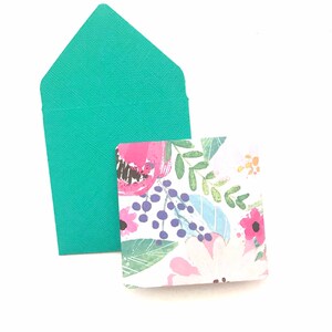 May include: A teal envelope with a floral patterned card inside. The card has pink, blue, and green flowers on a white background.