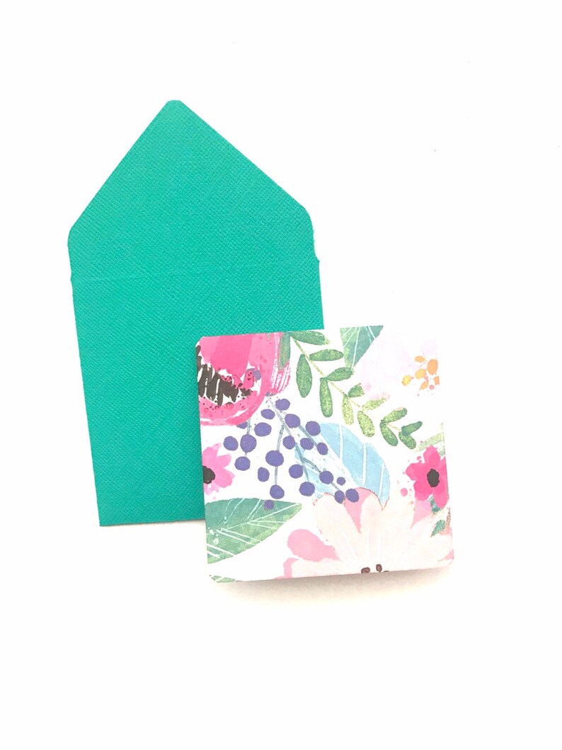 May include: A teal envelope with a floral patterned card inside. The card has pink, blue, and green flowers on a white background.
