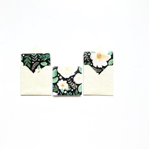 May include: Three white envelopes with floral designs on the front. The envelopes are on a white background.