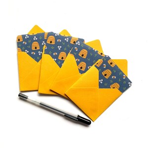 May include: Set of five yellow envelopes with a blue and yellow beehive pattern. The envelopes are folded and stacked on a white surface.