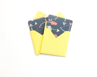May include: Two yellow envelopes with a blue and white patterned design featuring arrows and feathers. The envelopes are folded and stacked on top of each other.