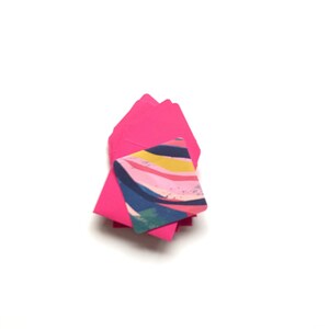 Op de afbeelding: Een stapel roze enveloppen met een kleurrijk abstract ontwerp op de bovenste envelop.