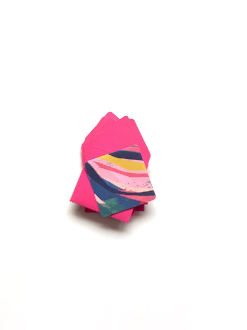 Op de afbeelding: Een stapel roze enveloppen met een kleurrijk abstract ontwerp op de bovenste envelop.