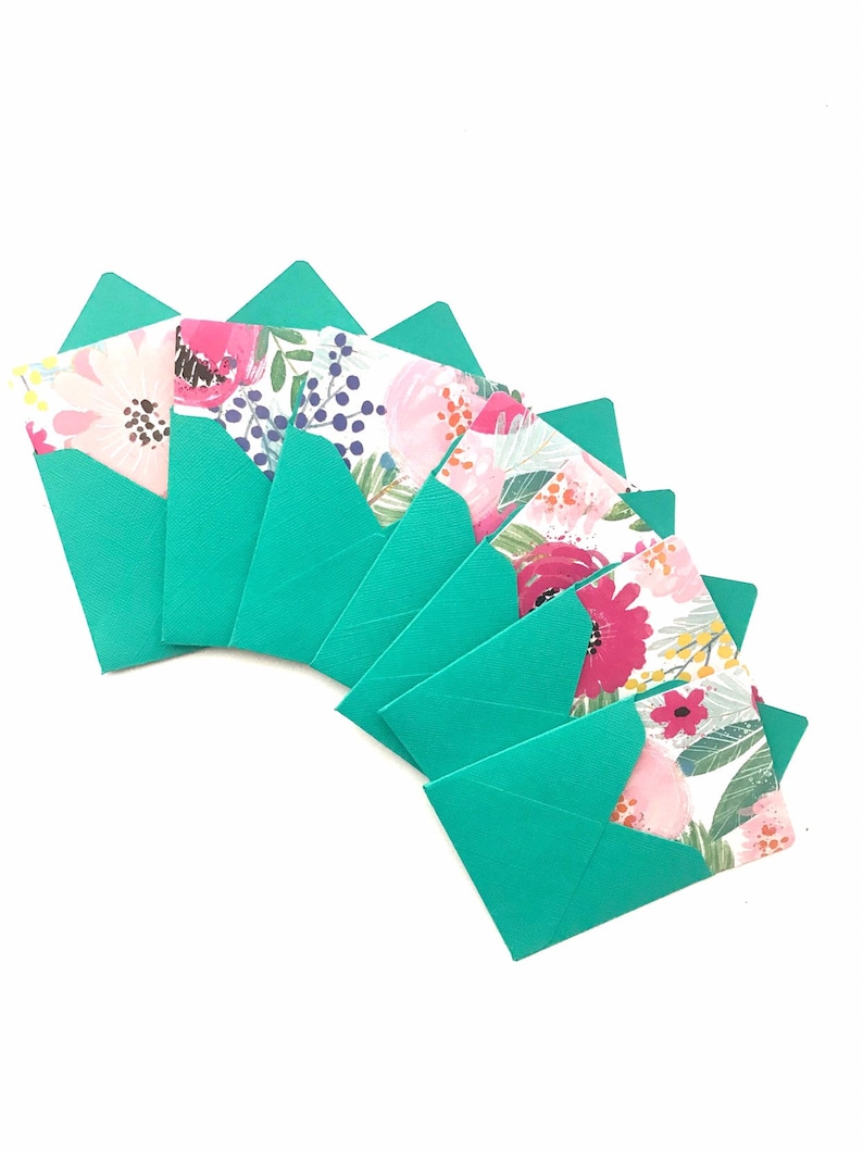 May include: A set of eight teal envelopes with floral patterns on the front. The envelopes are arranged in a fan shape.