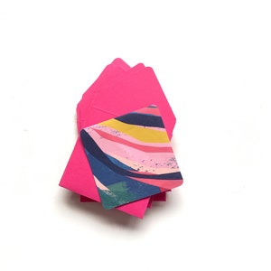 Op de afbeelding: Een stapel felroze enveloppen met een kleurrijk abstract ontwerp op de bovenste envelop.