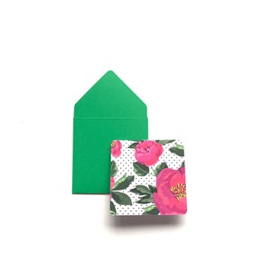 Op de afbeelding: Een groene envelop met een bloemenkaart erin. De kaart heeft een witte achtergrond met roze bloemen en zwarte stippen.