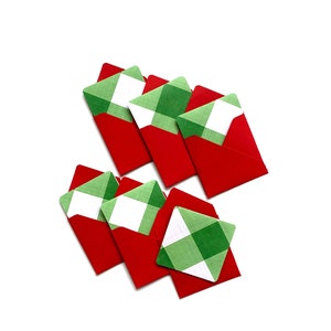 May include: A collection of red envelopes with green and white plaid patterned cards. The cards are partially visible, creating a festive and decorative arrangement. The envelopes are a solid red color.