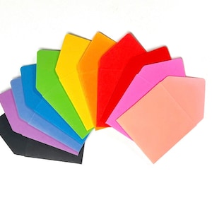 Puede incluir: Un conjunto de diez sobres coloridos en un patrón de arcoíris. Los sobres están dispuestos en forma de abanico, con el sobre negro en la parte inferior y el sobre rosa en la parte superior.