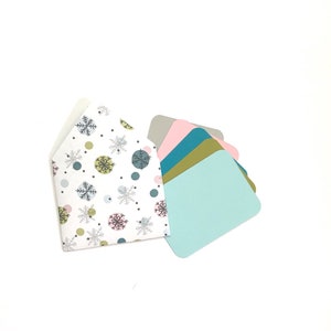 May include: A white envelope with a snowflake and polka dot pattern, with five blank cards in various colors: gray, pink, teal, gold, and light blue.