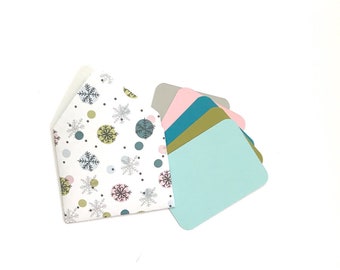 May include: A white envelope with a snowflake and polka dot pattern, with five blank cards in various colors: gray, pink, teal, gold, and light blue.
