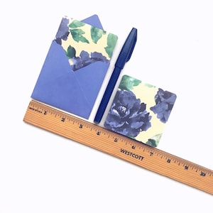 May include: A blue envelope with a floral patterned card inside. A blue pen and a wooden ruler are also in the image.