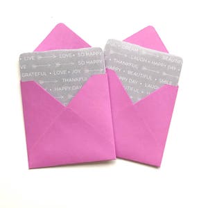 May include: Two pink envelopes with gray cards inside. The cards have a repeating pattern of arrows and positive words like "love", "happy", "joy", "grateful", "beautiful", "dream", "smile", and "laugh".