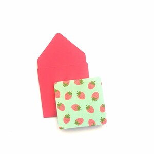Pode incluir: Um envelope rosa com um pequeno cart&atilde;o verde com um padr&atilde;o repetido de morangos vermelhos.