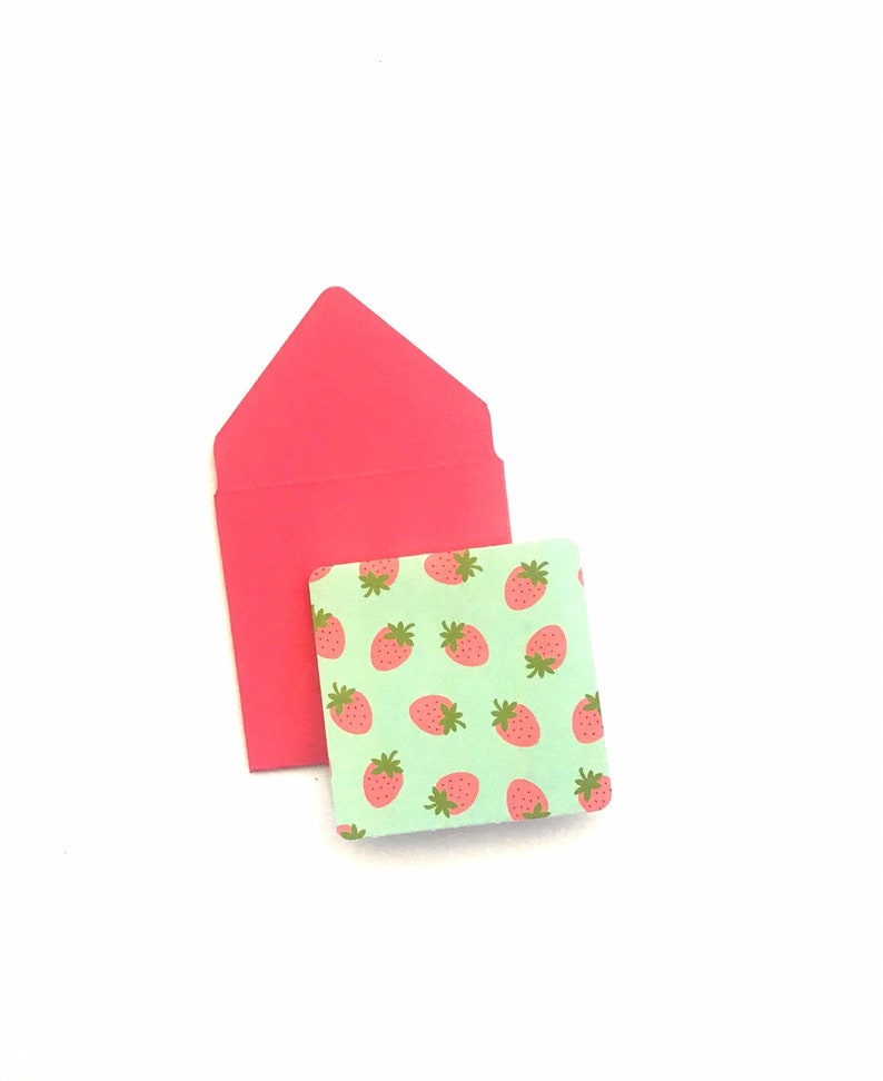 Pode incluir: Um envelope rosa com um pequeno cart&atilde;o verde com um padr&atilde;o repetido de morangos vermelhos.