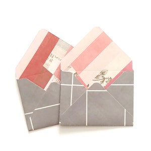 May include: Two gray envelopes with pink and white striped patterns on the inside. The envelopes have a white grid pattern on the outside.