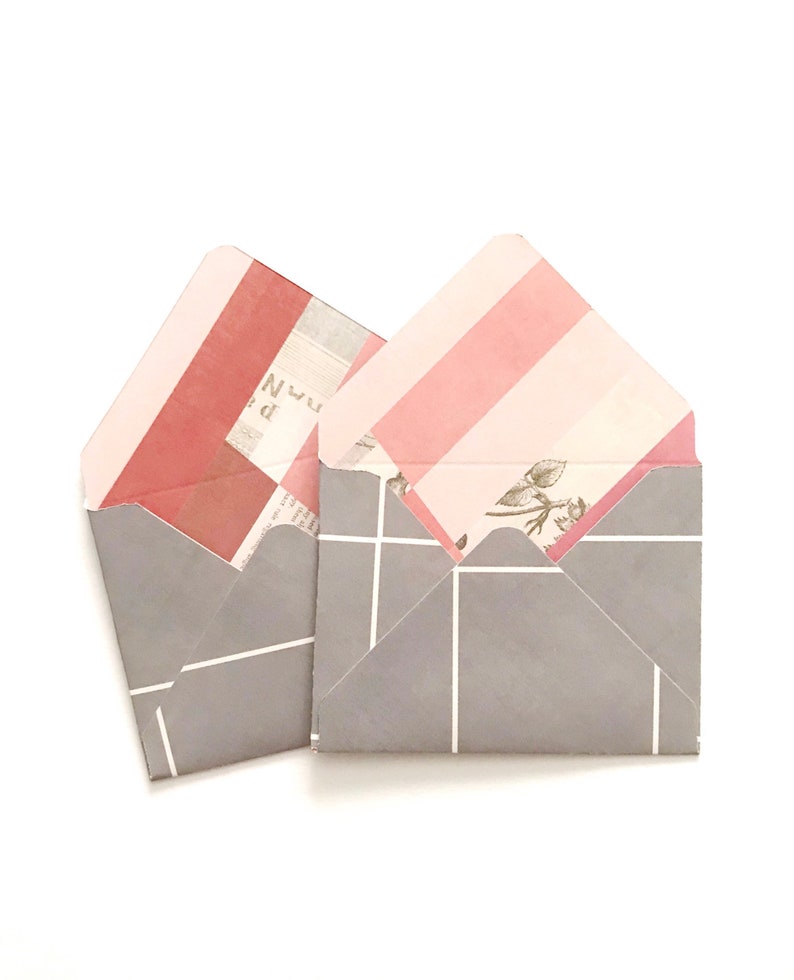 May include: Two gray envelopes with pink and white striped patterns on the inside. The envelopes have a white grid pattern on the outside.