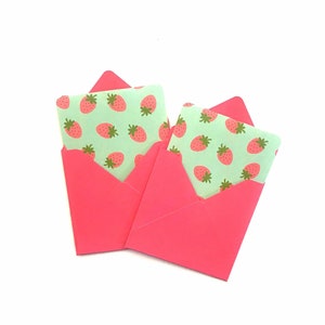 Pode incluir: Dois envelopes cor-de-rosa com um padr&atilde;o de morangos verdes e brancos na frente.