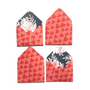 Peut inclure: Quatre petites enveloppes avec un motif de cœurs rouges. Les enveloppes sont doublées d'un motif floral sur fond noir.