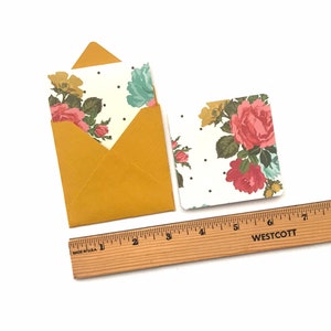 May include: A set of two floral note cards with envelopes. The cards have a white background with a pink, red, and green floral pattern and white polka dots. The envelopes are a mustard yellow colour.