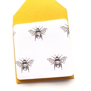 May include: A yellow envelope with a white card inside. The card has a repeating pattern of black and white bee illustrations.