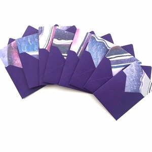 Puede incluir: Un conjunto de ocho sobres morados con una variedad de diseños abstractos impresos en el interior. Los diseños presentan tonos de azul, rosa y blanco.