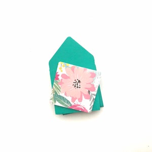 May include: A stack of teal envelopes with a floral patterned card on top. The card features a pink flower with a dark center and green leaves.