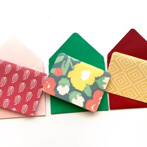Könnte beinhalten: Drei gefaltete Umschläge mit verschiedenen gemusterten Karten darin. Die Umschläge sind rosa, grün und rot. Die Karten haben Blumen-, geometrische und Paisley-Muster.