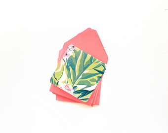 Op de afbeelding: Een stapel roze enveloppen met een kaart met een groen en wit bloemenpatroon erop.
