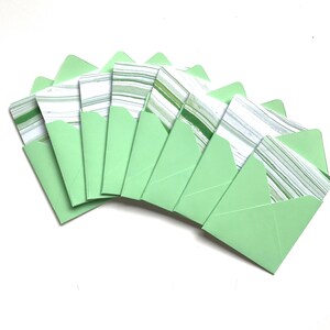 Puede incluir: Un juego de ocho sobres verdes con insertos de papel marmoleado blanco y verde.