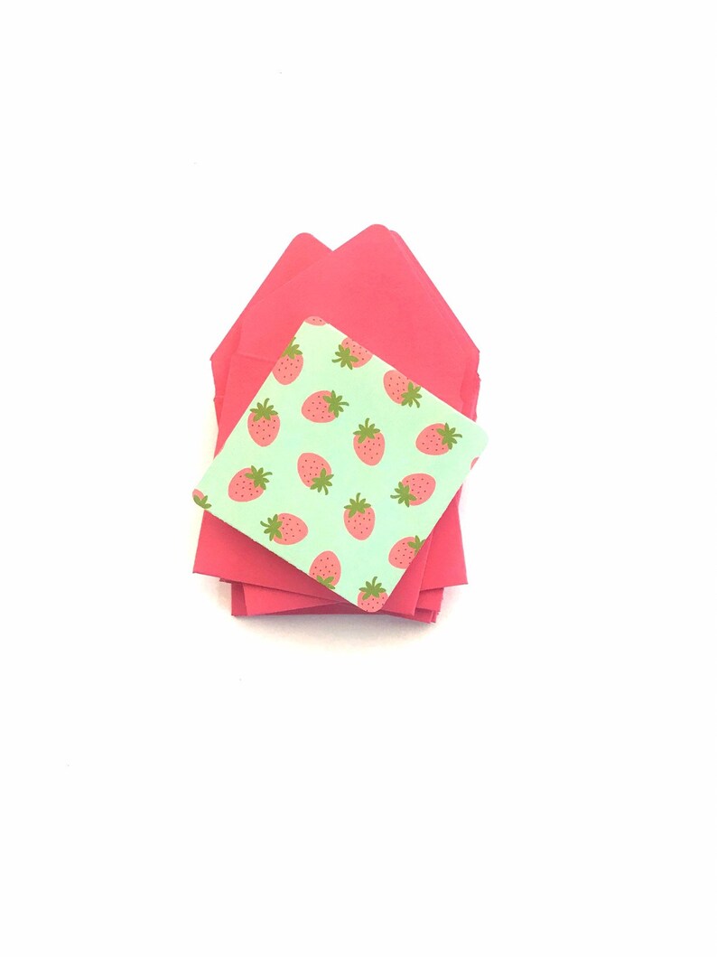 Pode incluir: Uma pilha de envelopes cor-de-rosa com um pequeno envelope verde com um padr&atilde;o de morangos no topo.