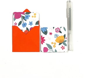 May include: A set of two small cards with a floral pattern. The cards are white with colorful flowers and green leaves. The cards are in a bright orange envelope.