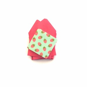 Pode incluir: Uma pilha de envelopes cor-de-rosa com um envelope verde com um padr&atilde;o de morangos no topo.