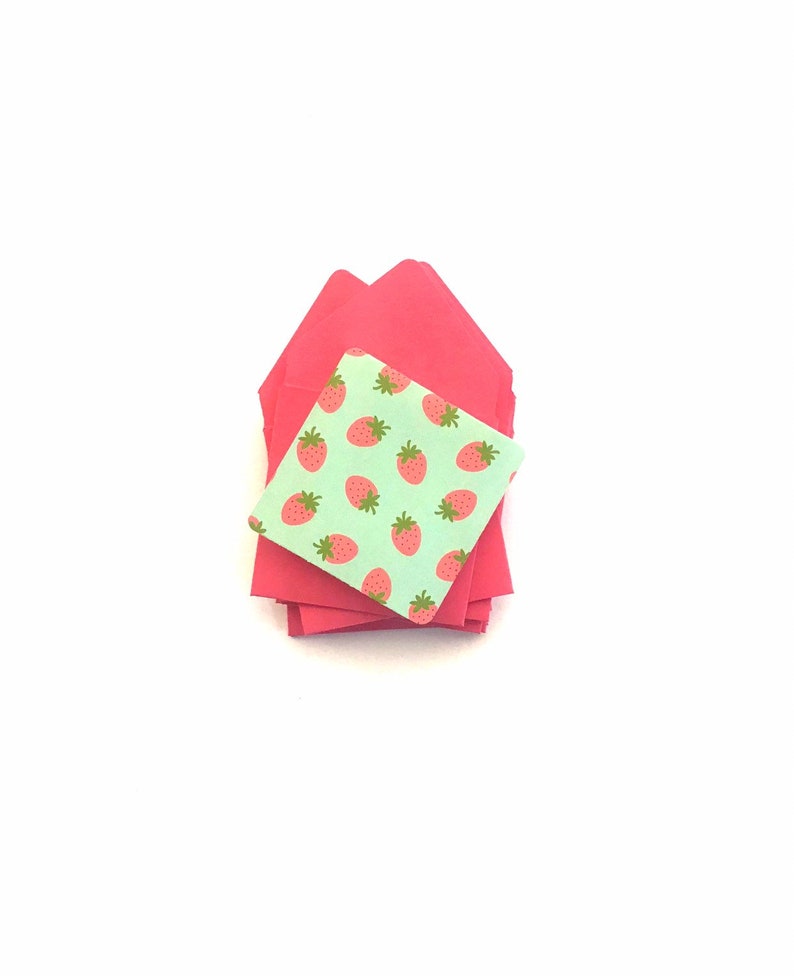 Pode incluir: Uma pilha de envelopes cor-de-rosa com um envelope verde com um padr&atilde;o de morangos no topo.