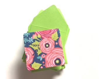 May include: A stack of lime green envelopes with a floral patterned card on top. The card features pink, blue, and green flowers on a dark blue background.