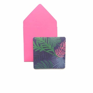 Puede incluir: Un sobre rosa con una tarjeta cuadrada dentro. La tarjeta tiene un patr&oacute;n de hojas tropicales en tonos de verde, azul y rosa sobre un fondo azul oscuro.