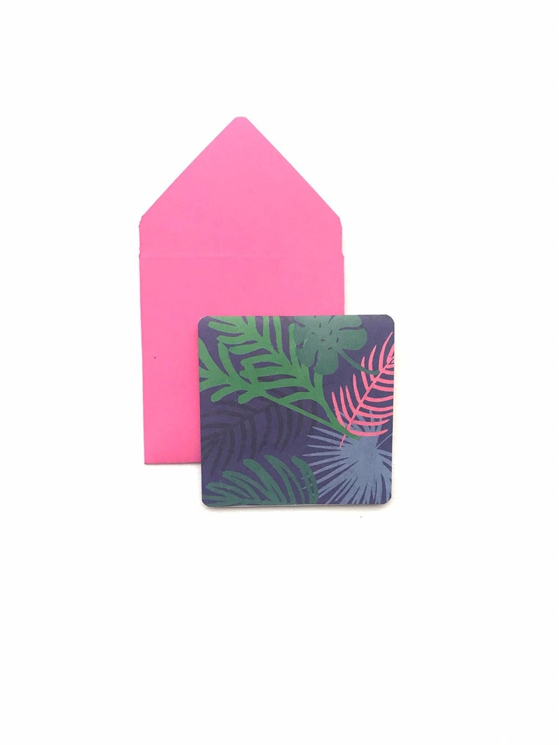 Puede incluir: Un sobre rosa con una tarjeta cuadrada dentro. La tarjeta tiene un patr&oacute;n de hojas tropicales en tonos de verde, azul y rosa sobre un fondo azul oscuro.
