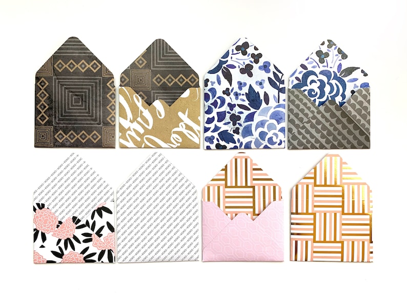 Puede incluir: Ocho sobres con diferentes patrones, incluyendo dise&ntilde;os geom&eacute;tricos, florales y a rayas. Los sobres son de varios colores, incluyendo negro, blanco, azul, rosa y dorado.