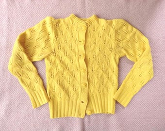 May include: A bright yellow long-sleeve cardigan featuring a repeating diamond-shaped openwork knit pattern. The garment has a crew neckline, ribbed cuffs, a ribbed hem, and a front button closure with matching yellow circular buttons.