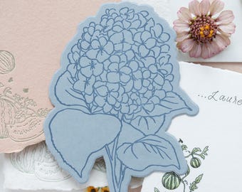 Segnaposto con motivo ortensia, stampati a rilievo, fustellati, su cartoncino blu o bianco, con nomi calligrafici.