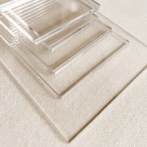 May include: Four clear acrylic squares stacked on top of each other on a white textured surface.