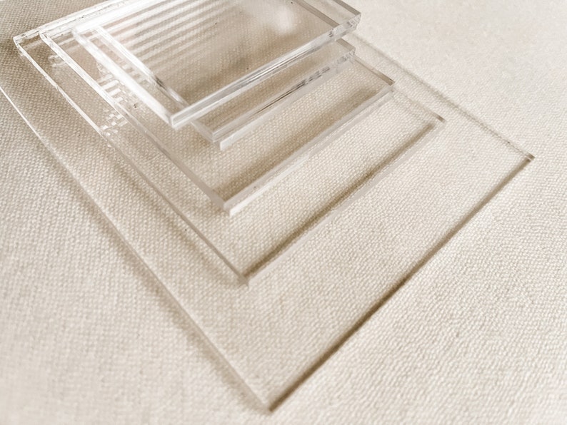 May include: Four clear acrylic squares stacked on top of each other on a white textured surface.