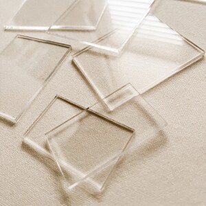 May include: A group of clear acrylic squares of various sizes stacked on top of each other. The squares are arranged in a random pattern and are slightly overlapping.