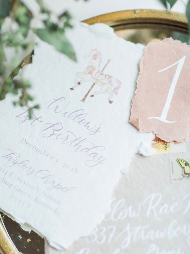 May include: A white card with purple calligraphy that reads "Willow's 1st Birthday" and "December 1, 2015" and "Taylor's Chapel" and "271 L. Seventh Avenue" and "Bowling Green, Kentucky" and "42141". A pink card with white calligraphy that reads "1" is on top of the white card.
