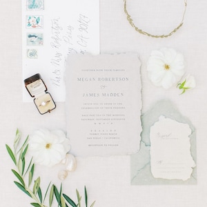 May include: Wedding invitation suite with a white background and blue and green accents. The invitation features the names Megan Robertson and James Madden, the date and time of the wedding, and the location. The RSVP card is also included.