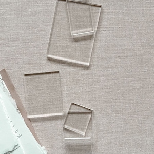 May include: Four clear acrylic display stands of varying sizes. The stands are rectangular and have a smooth, polished finish.