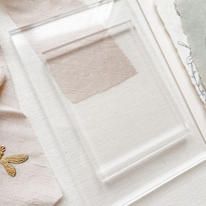 May include: A clear acrylic display stand with a raised platform. The stand is designed to hold and display small items, such as jewellery, cards, or other decorative objects.