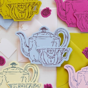 Può includere: Un assortimento di ritagli di carta colorati di teiere e tazze da tè in giallo, rosa e blu, con buste abbinate e adesivi a forma di lampone. È incluso anche un cartellino vuoto.