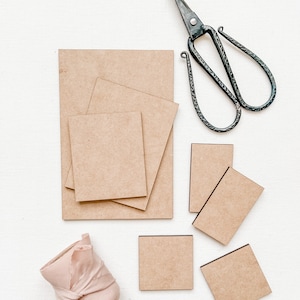 May include: A set of six brown cardboard squares of varying sizes, a pair of black metal scissors, and a roll of pink fabric ribbon.
